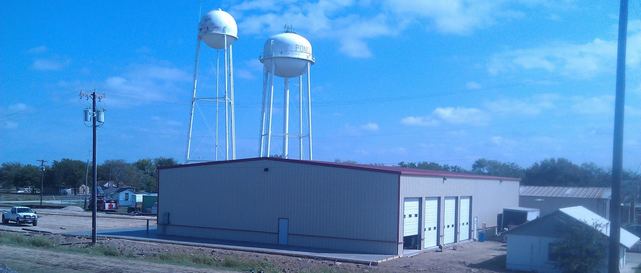 Industrial building with three large water towers labeled 'POND' behind it, power lines and a few vehicles in the background.