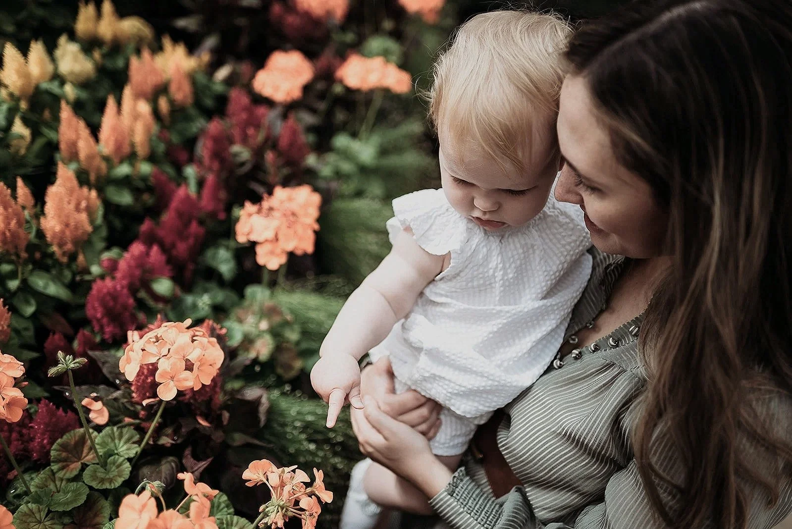 A woman holding a young girl among colorful flowers.