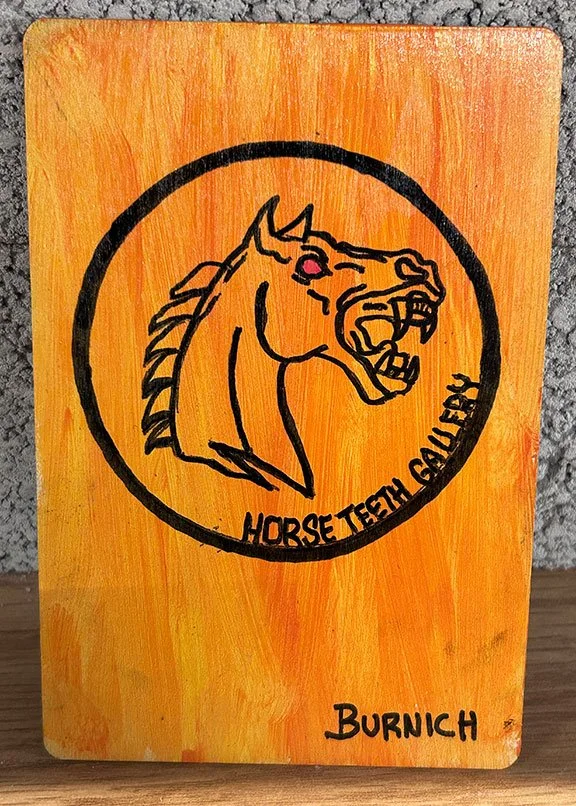 Painted wooden sign with a black outline of a horse's head, featuring a pink eye, and text reading 'HORSE TTEETH GALLERY' and 'BURNICH' on an orange and yellow background.