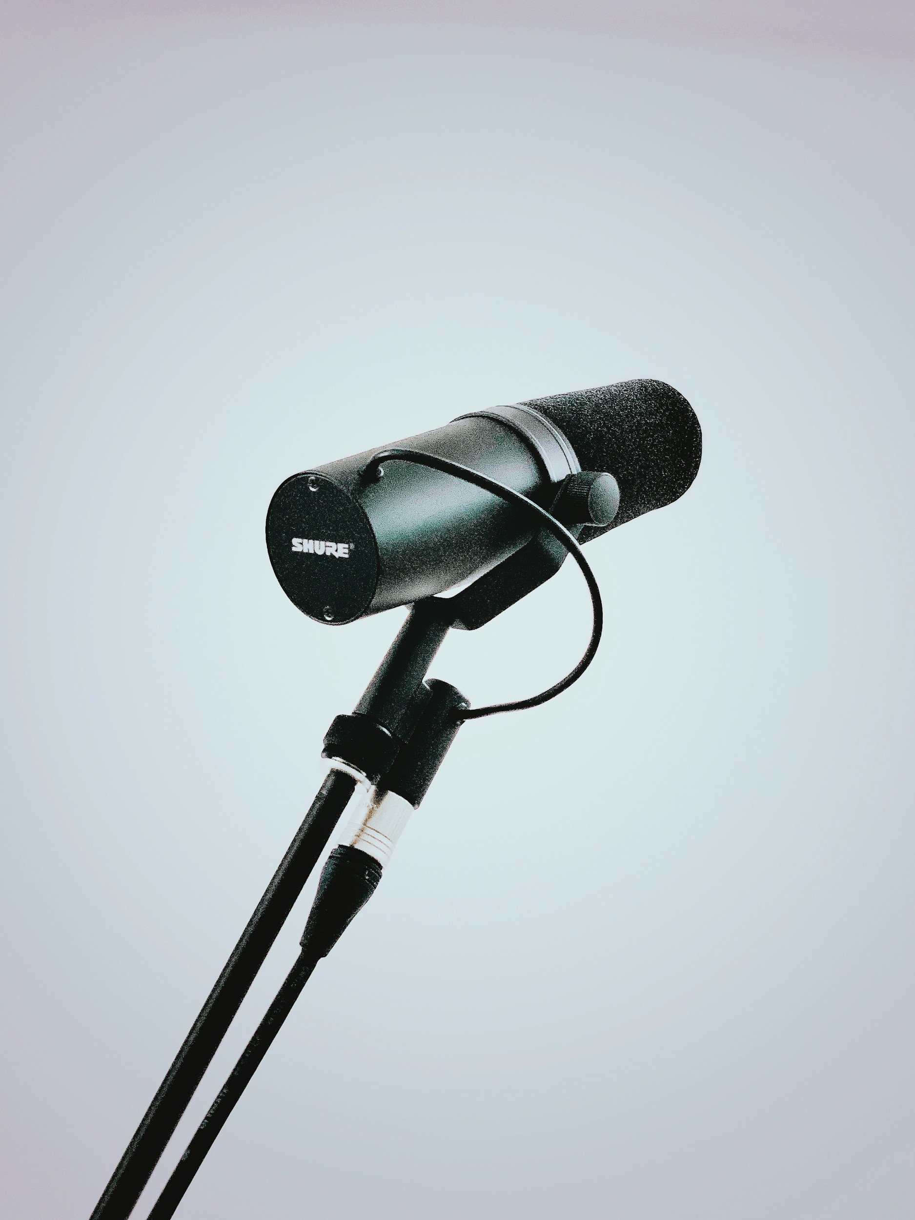 A Shure microphone mounted on a stand against a light background.