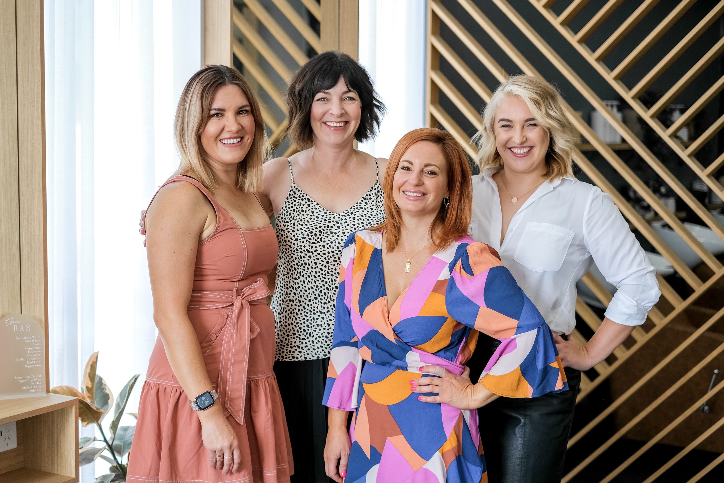 Five women standing together indoors, smiling at the camera.