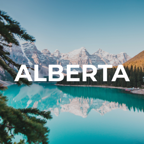 Scenic view of alpine mountains with snow, a clear blue lake, and a forested area in Alberta.
