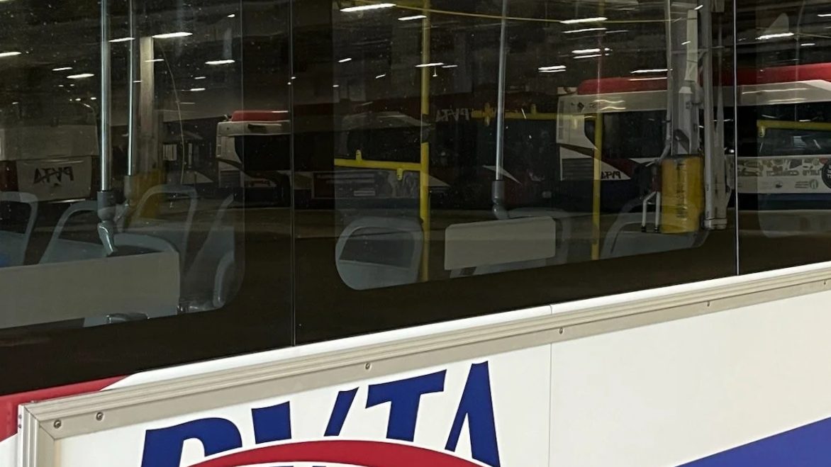 A reflective window showing empty chairs and buses inside a bus depot, with part of a sign visible in the foreground.