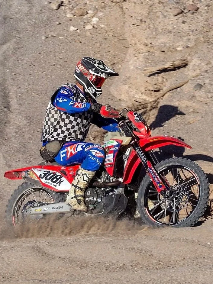 Motocross rider in racing gear riding a red dirt bike on a dirt track.