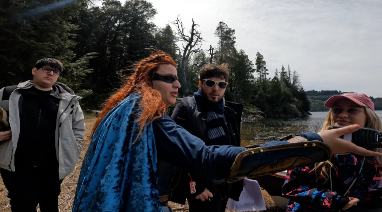 Grupo de cuatro personas disfrutan de un tour en naturaleza junto a un lago, con árboles y cielo nublado en el fondo.