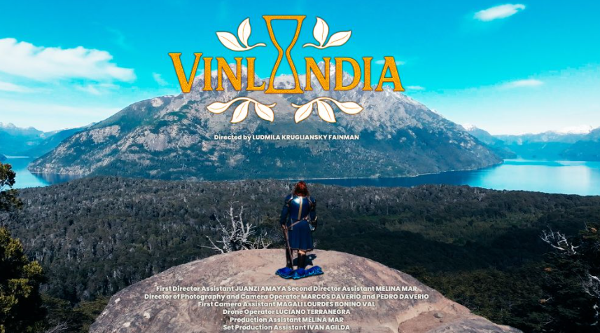 Una persona con ropa tradicional en un mirador sobre un paisaje de montañas y agua, el título 'Vinlandia' en la parte superior, y texto de créditos debajo.