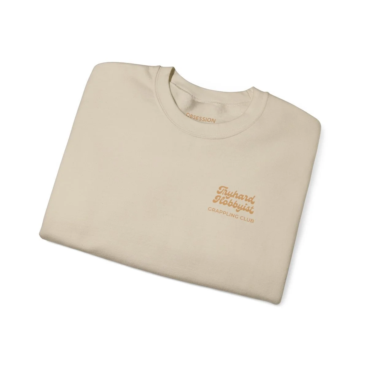 Cream-colored T-shirt folded with orange text that reads 'Tryhard Hobbyist Grappling Club' on the front.