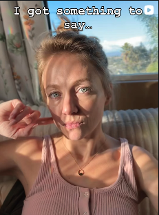 The poet, T.L. Amber, with blond hair and blue eyes sitting indoors, wearing a pink tank top,  with sunlight on her face, and a window with curtains and trees visible in the background, with text overlay that says 'I have something to say...'