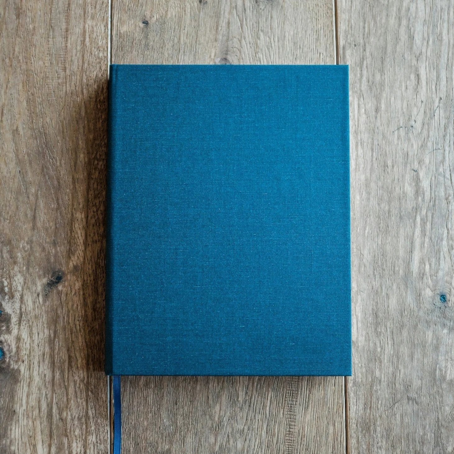 A closed blue hardcover notebook with a matching bookmark ribbon on a wooden surface, representing custom poetry by T.L. Amber.