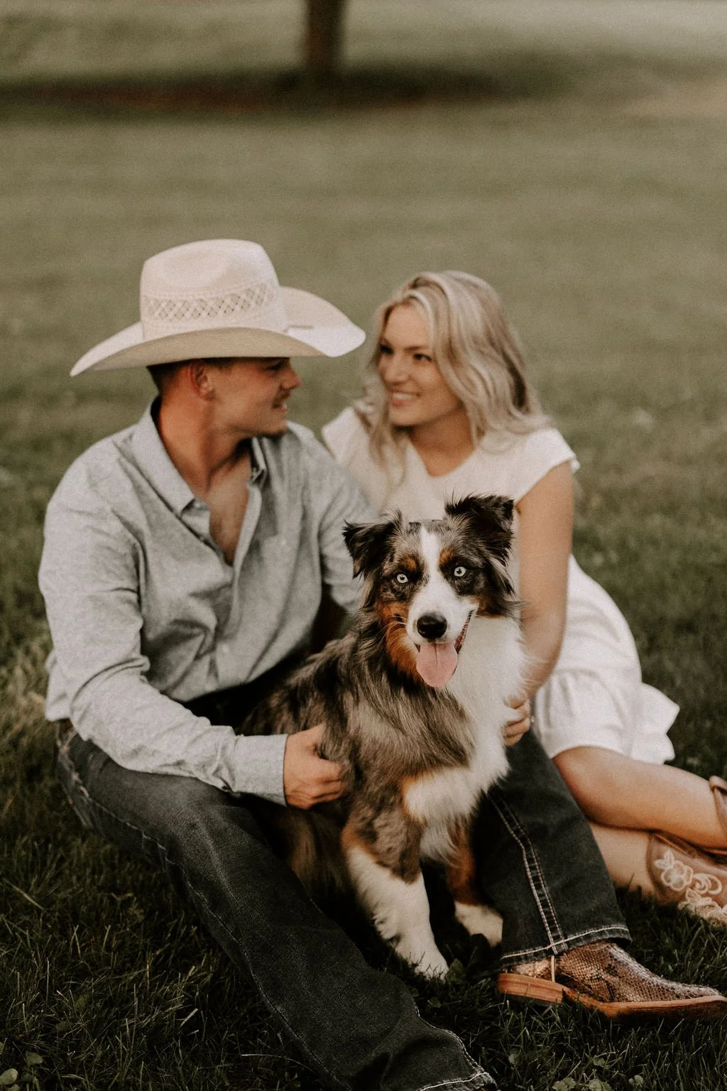 Couple looking at eachother while sitting with their dog in the yard