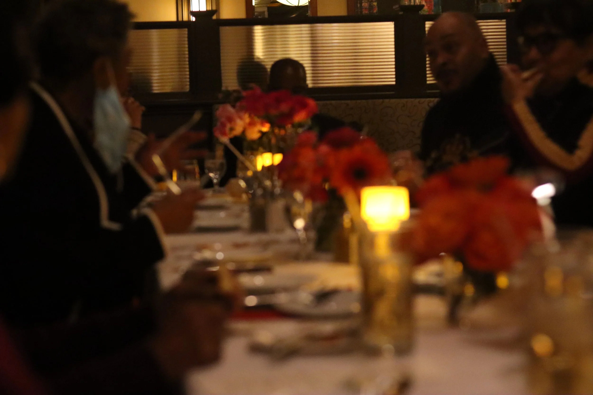 People dining at a dimly lit restaurant table decorated with flowers and candles, engaging in conversation.