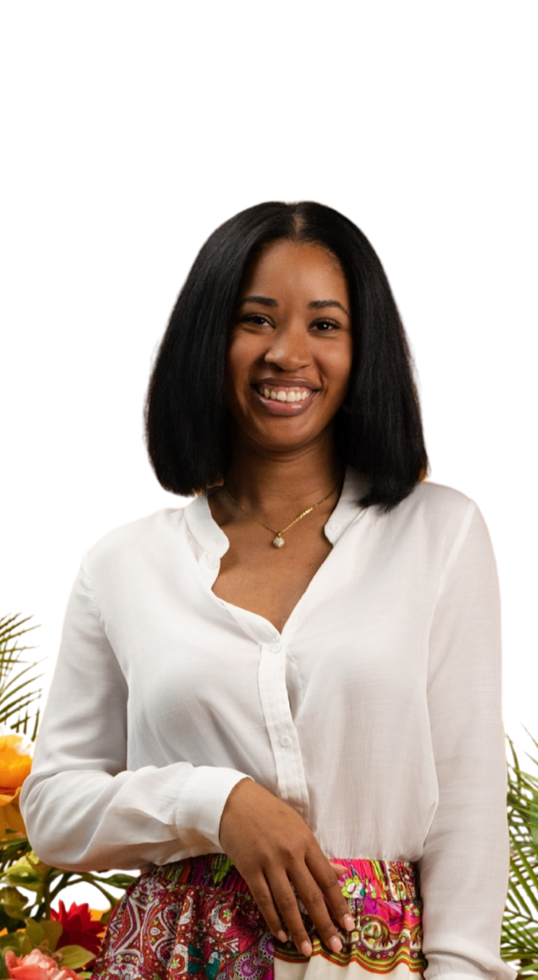 A smiling woman with shoulder-length black hair wearing a white blouse and colorful patterned skirt, standing beside a bouquet of flowers.