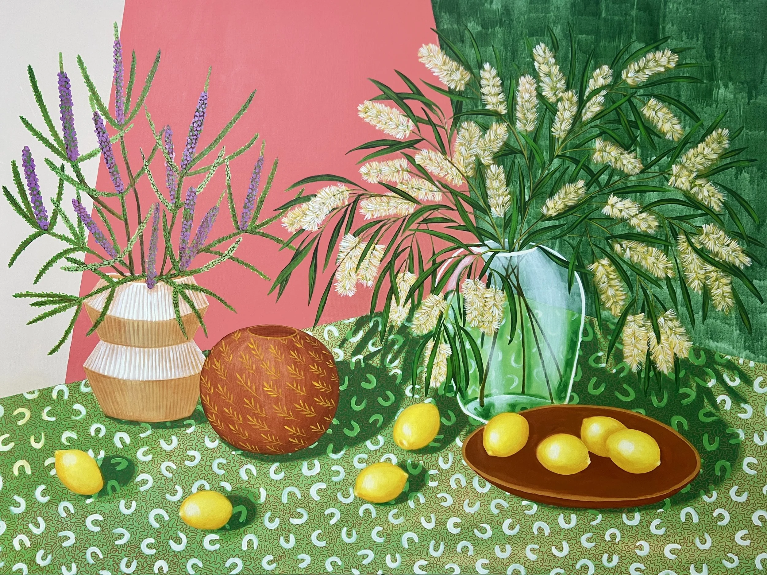 A contemporary still life painting of vases filled with blooming Australian melaleuca, lemons scattered across the green and white patterned tablecloth,  with a pink and green background.