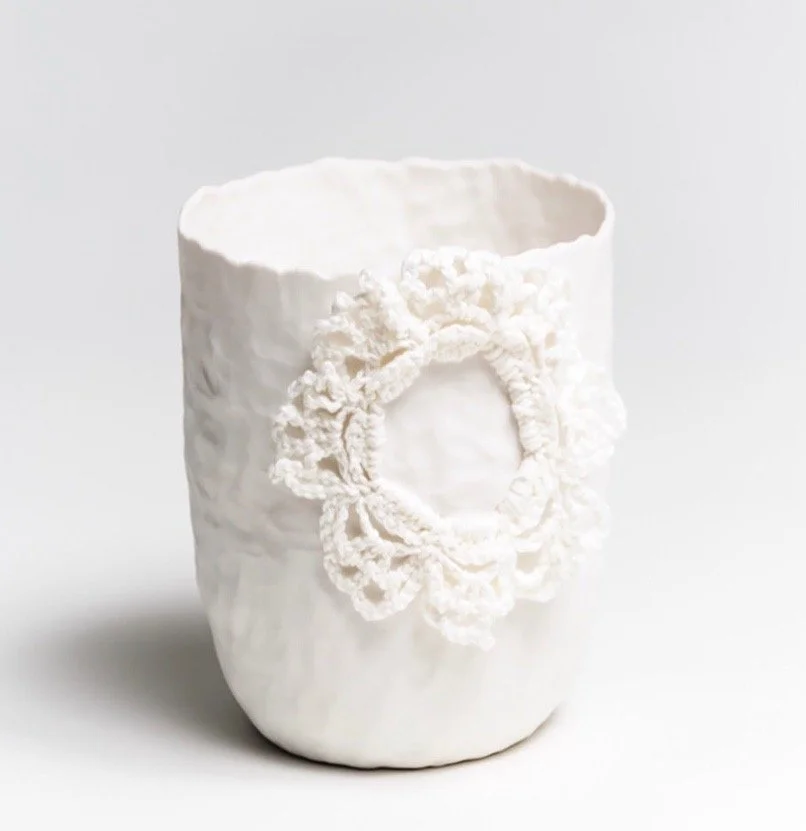 A handbuilt white porcelain vase with a textured surface and a decorative circular crochet detail on the front, against a plain white background.