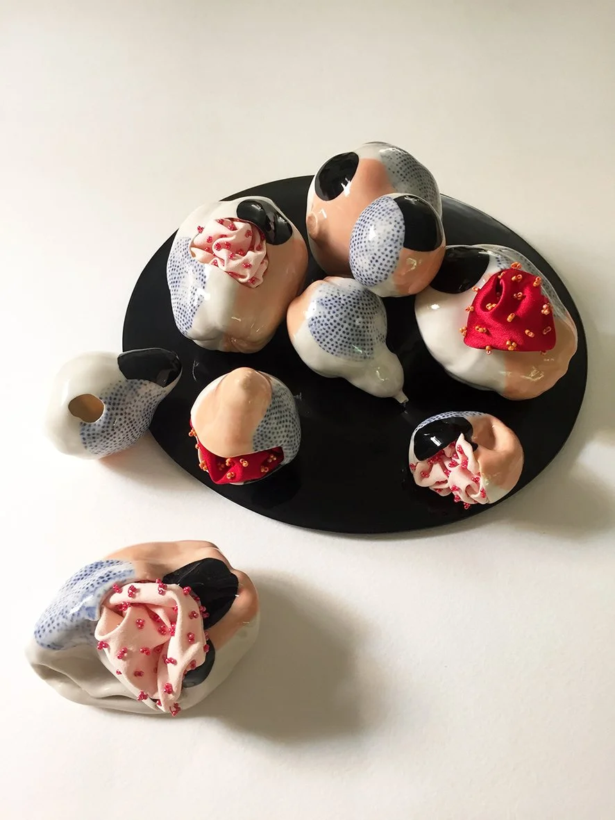 Slip cast porcelain fruit are highly decorated with pattern and a colour scheme of black, pink, white, red and blue, are placed on a black tray and a white surface.