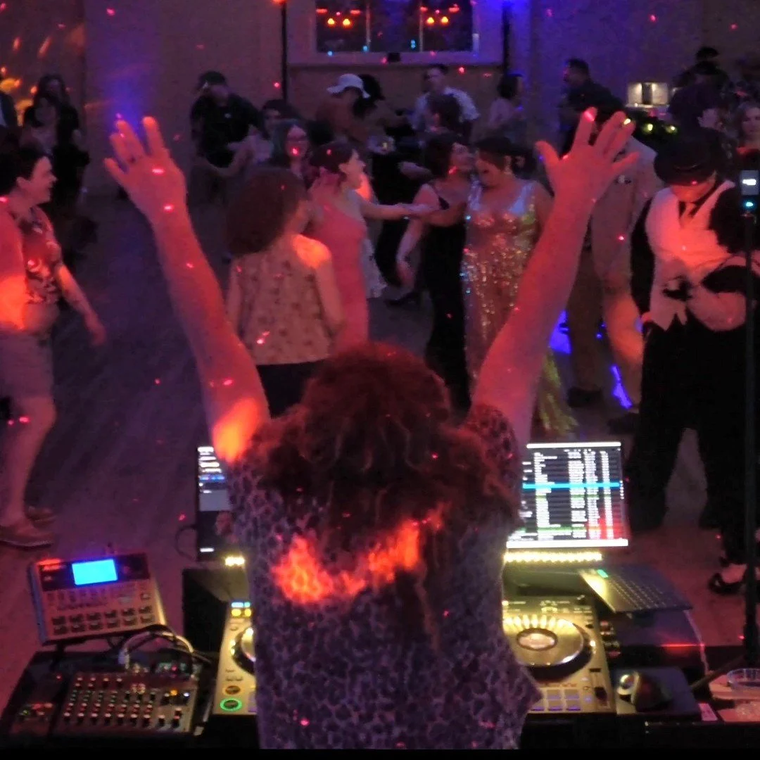 DJ performing at a nightclub with people dancing and socializing on the dance floor.