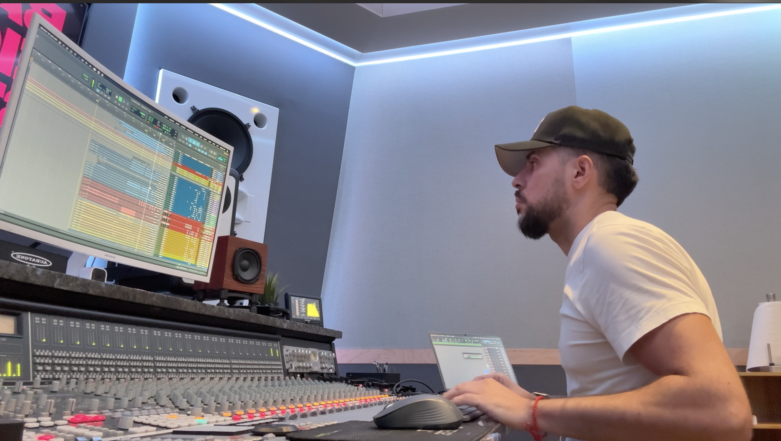 Hombre en estudio de grabación con consola de sonido y computadora, trabajando en producción musical.