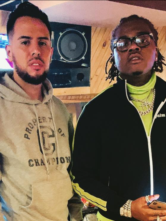 Dos hombres en un estudio de grabación, uno con sudadera beige y el otro con chaqueta negra, lentes, y varias cadenas de oro.