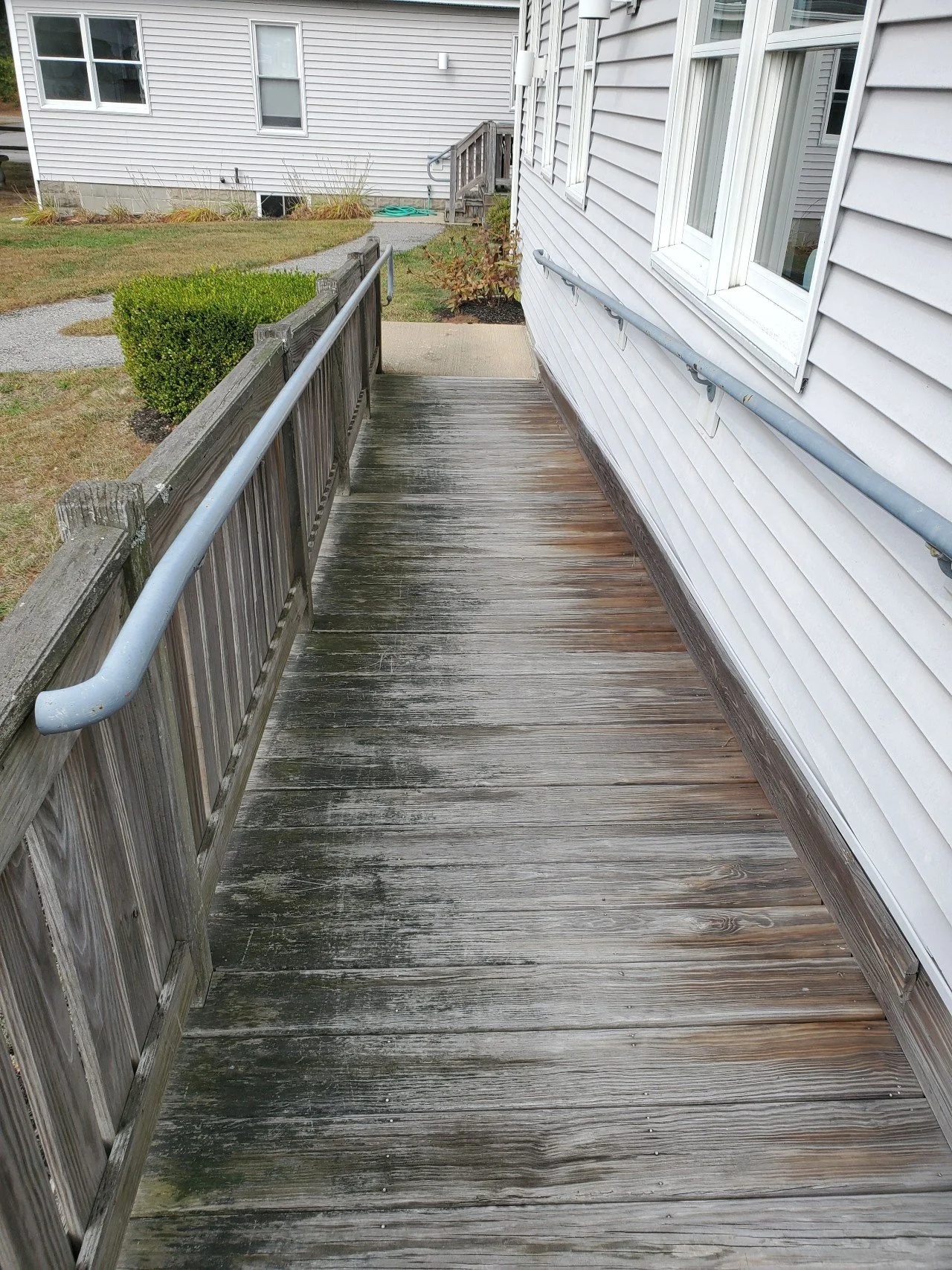 before photo wooden handicap ramp with a weathered surface, side rails, and a local business on the right, leading to a sidewalk and yard in the background.