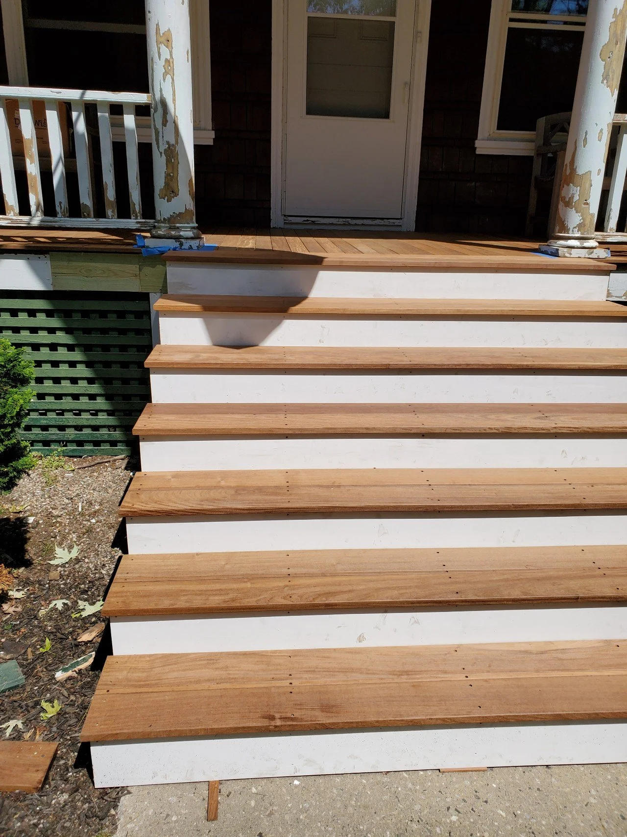 New mahogany stairs being installed outside a house, with a white railing and door in the background.