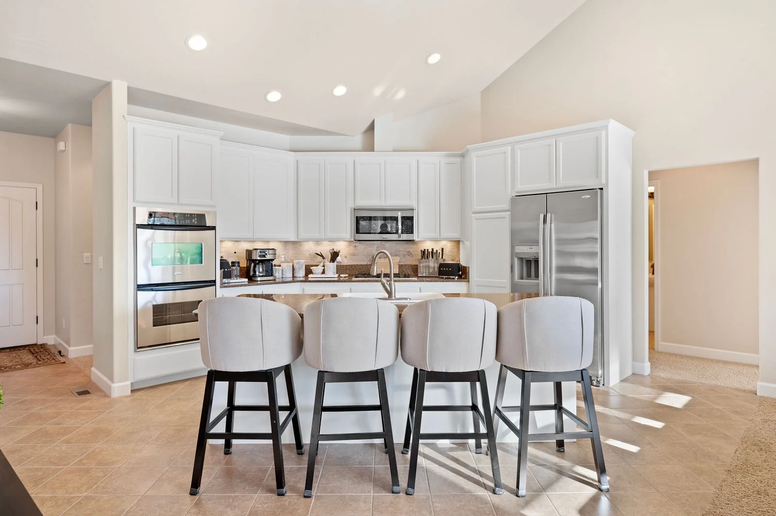 Professional photograph of a straight on of a white kitchen with four barstools