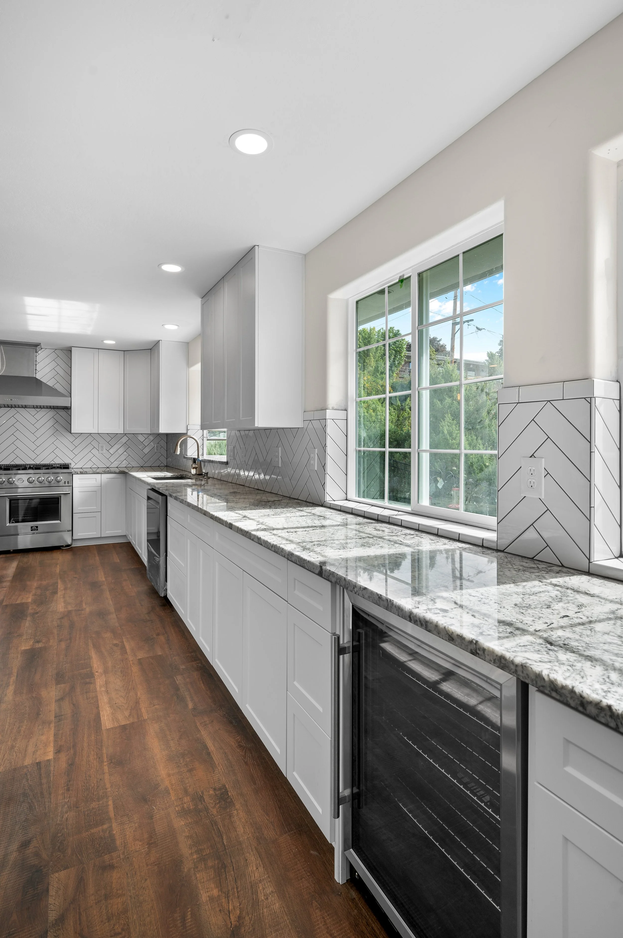 White kitchen with chevron tile backsplash and two windows. The sink and new appliances are stainless steal and new.