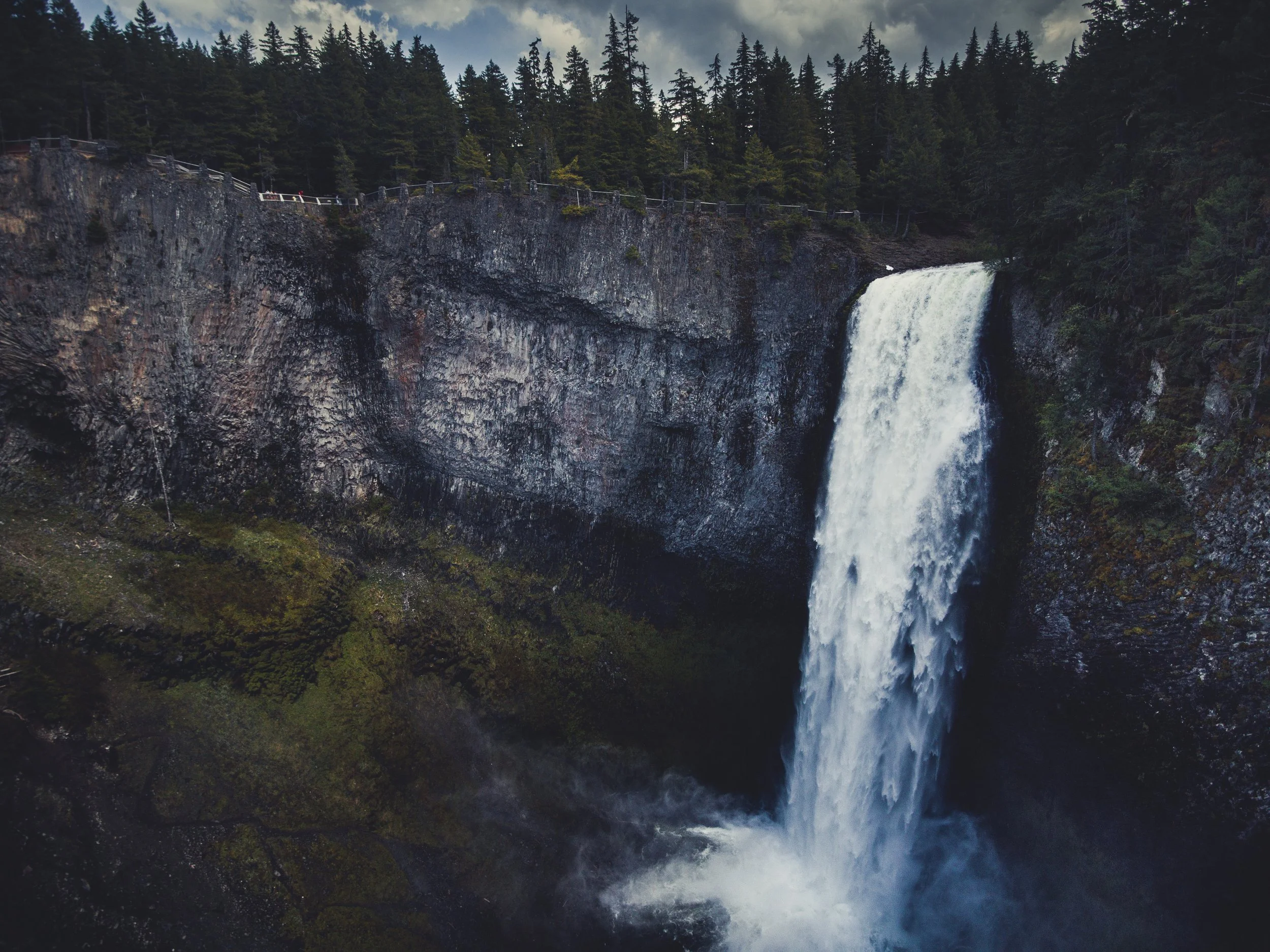 A tall waterfall cascading over a rocky cliff surrounded by evergreen trees.