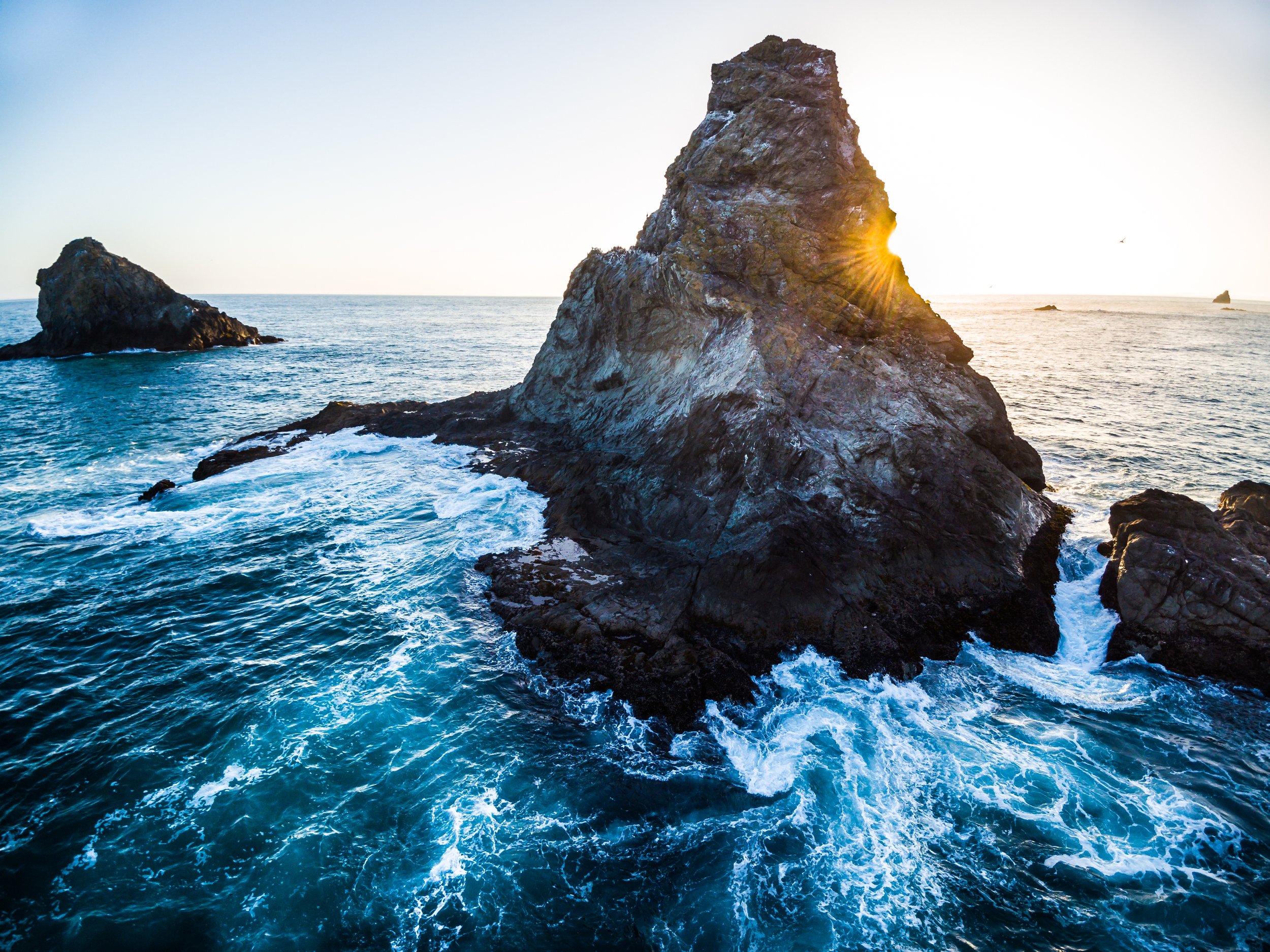 Sunset over ocean with large rock formations in water.