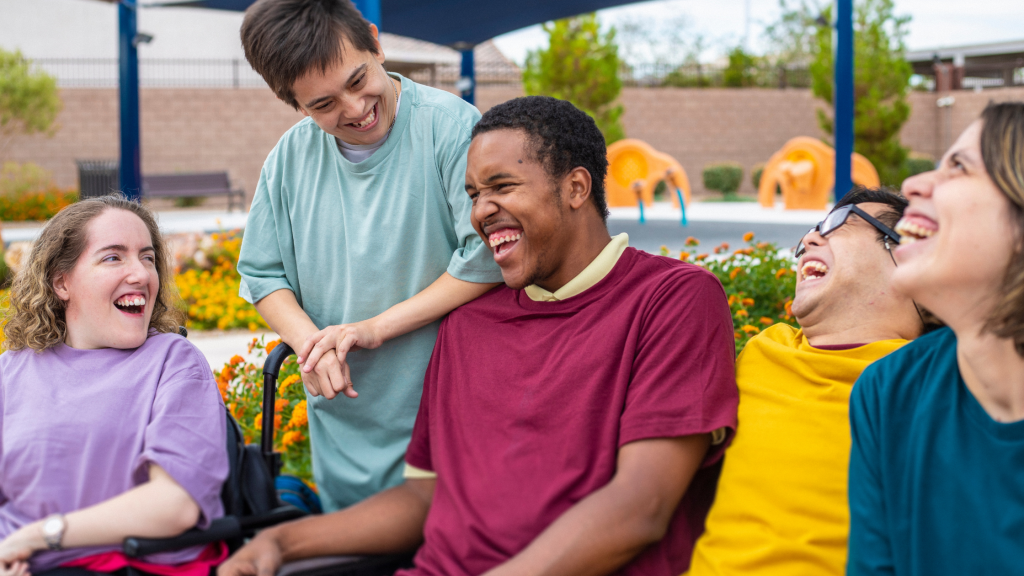 Group of five young adults with disabilities laughing and enjoying outdoor activity