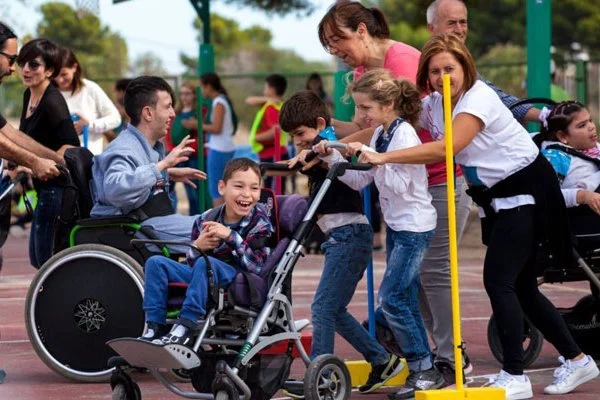 A group of children and adults at a skate park, some children in wheelchairs, laughing and engaging with each other.