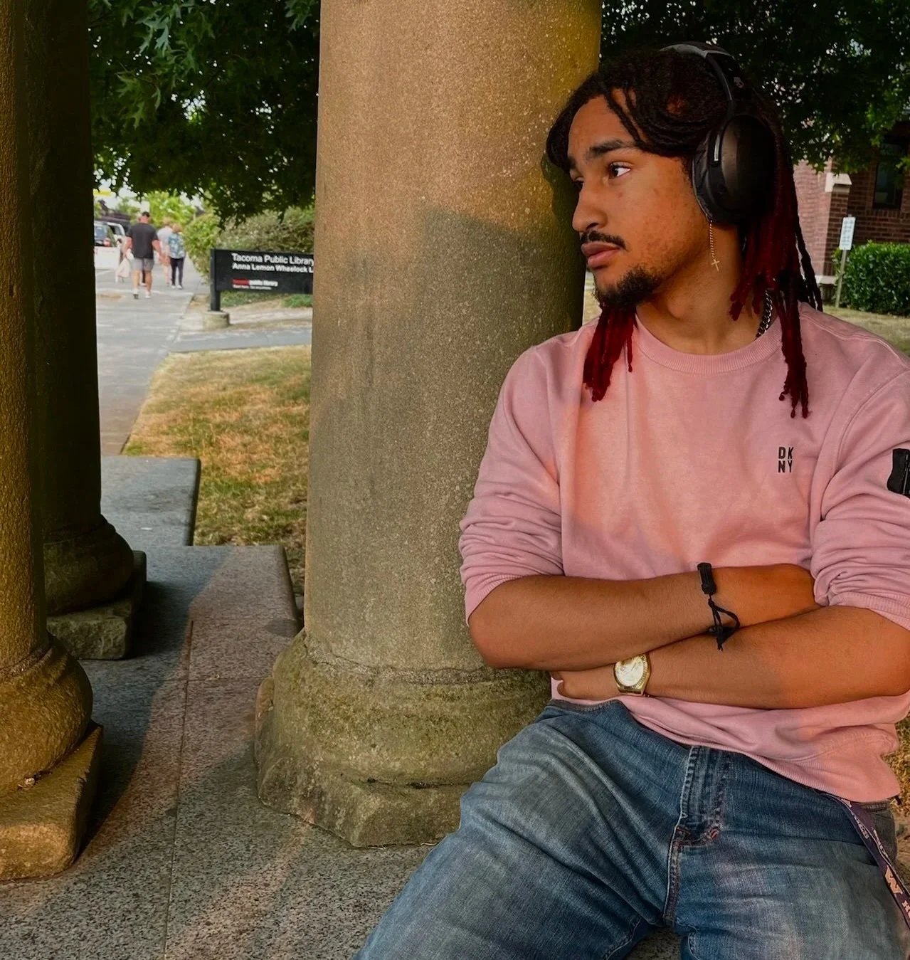 A man with curly dark hair, wearing clear eyeglasses and a nose ring, looking to the side, sitting indoors near a potted plant.