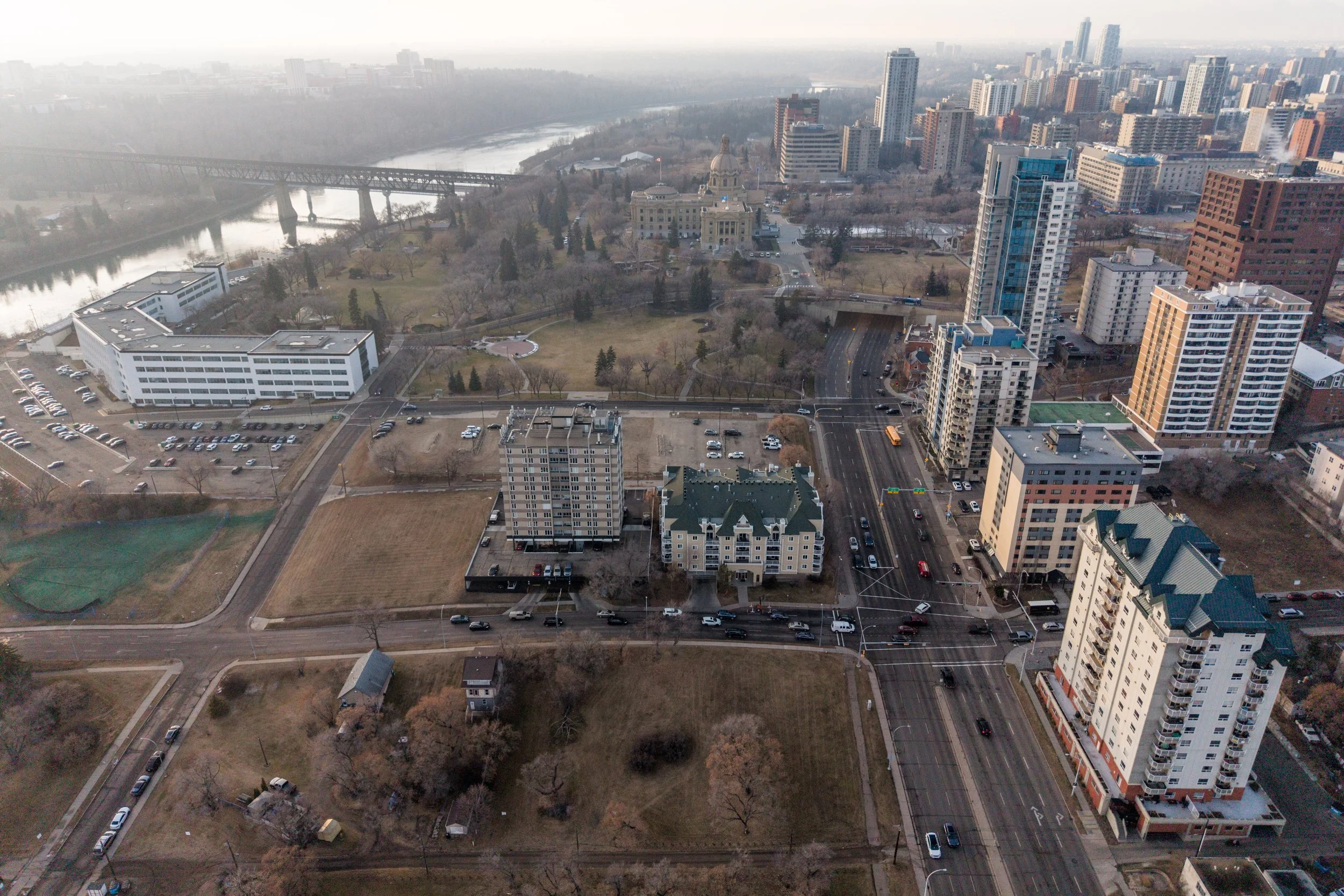 Aerial view of a cityscape with tall buildings, a river, and a park with trees and pathways.