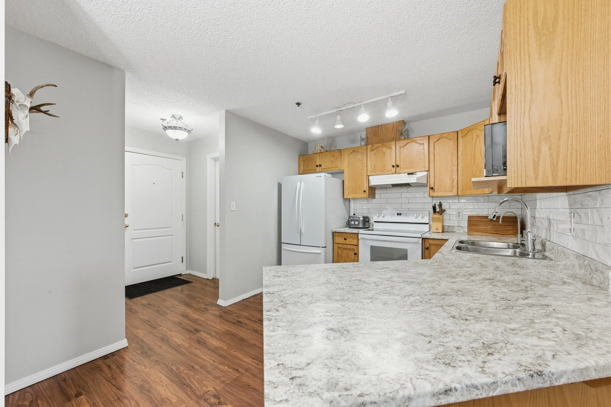 Kitchen with wooden cabinets, white appliances, granite countertop, and hardwood floors.