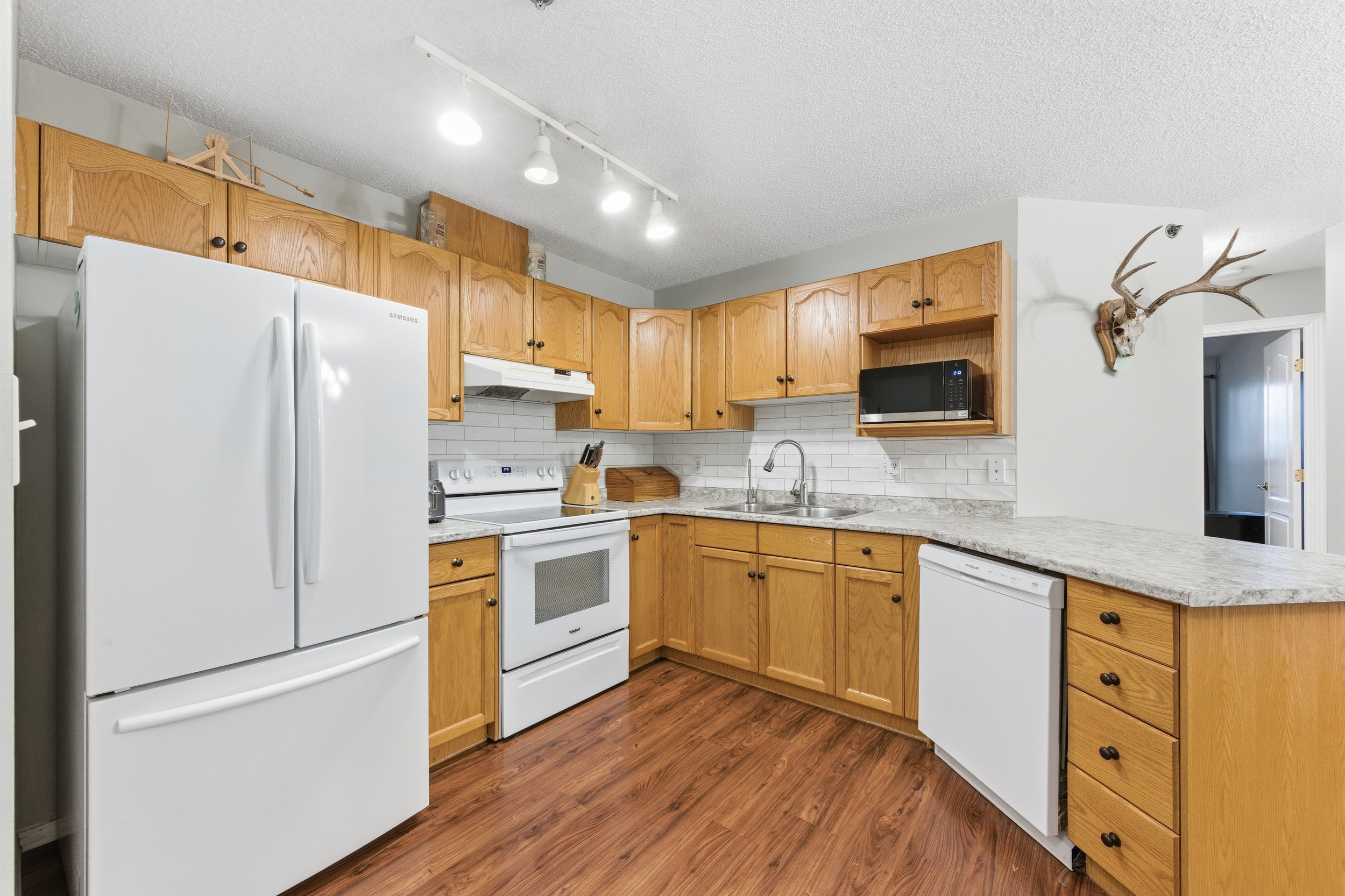 Kitchen with wooden cabinets, white appliances including refrigerator, oven, and microwave, and a granite countertop. A deer skull with antlers is mounted on the wall.