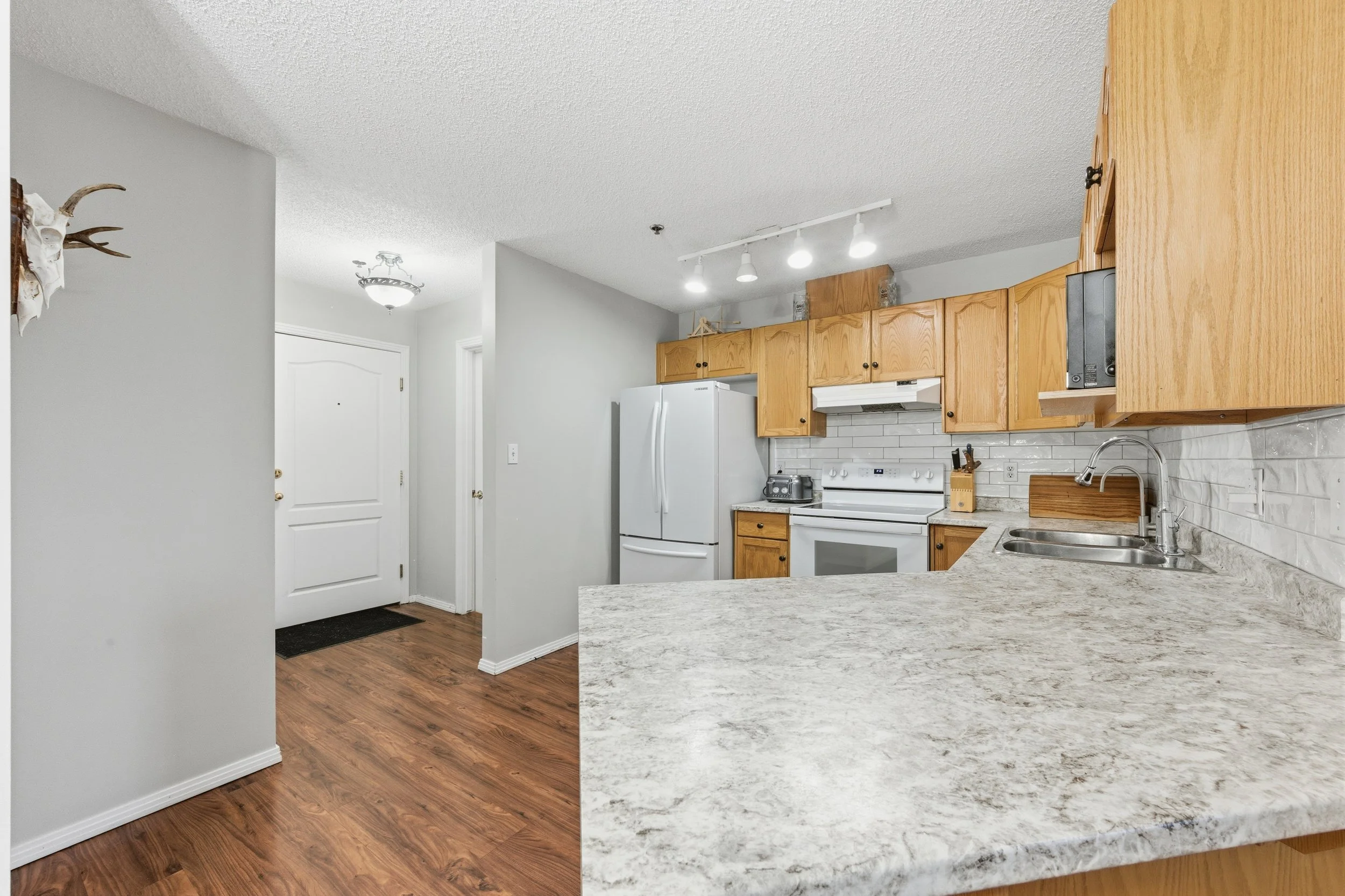 Kitchen with wooden cabinets, white appliances, marble countertop, and hardwood floors.