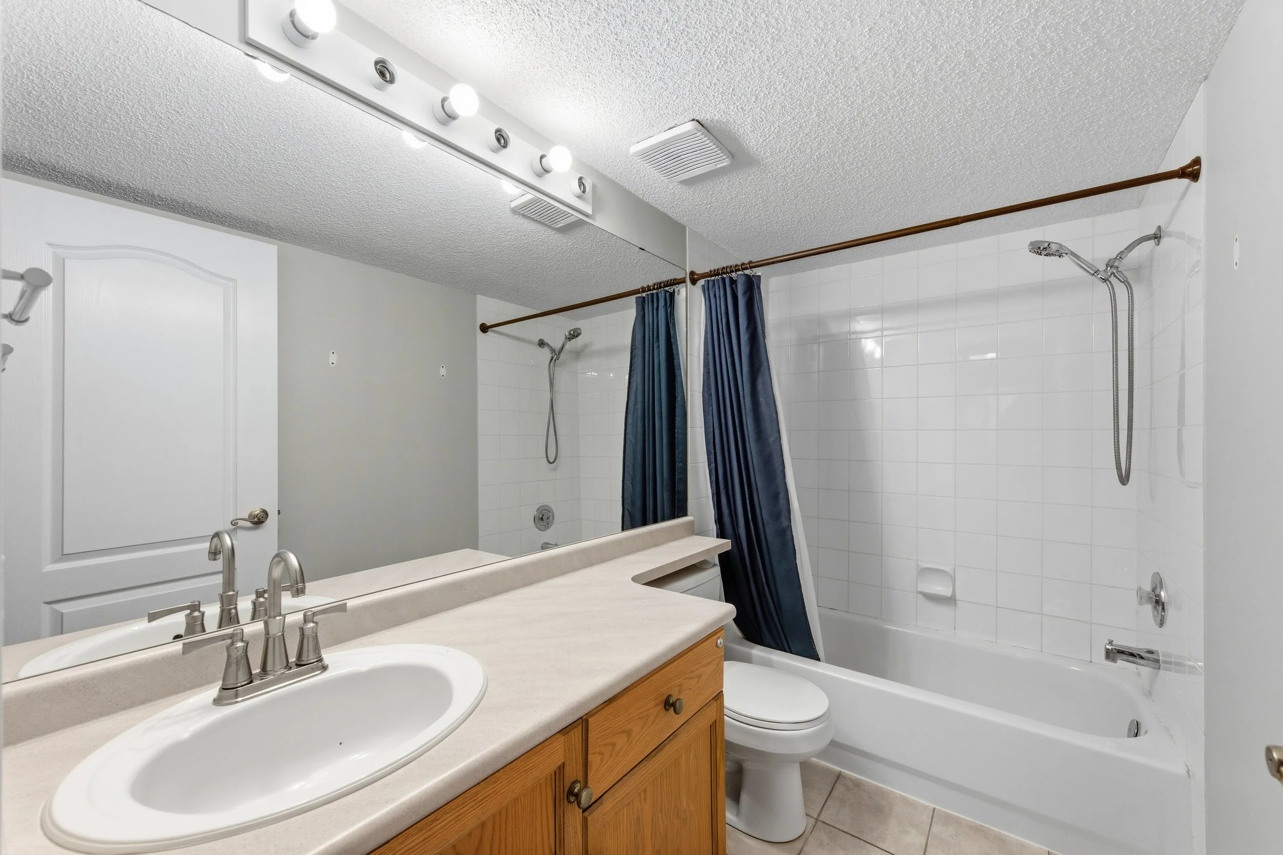 Bathroom with vanity, sink, mirror, toilet, bathtub with shower, and blue shower curtain.