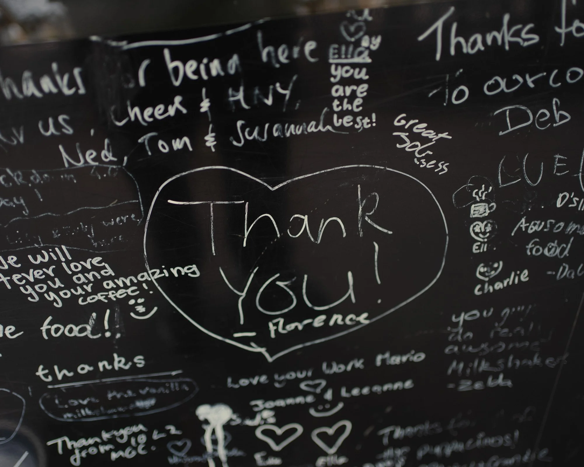Blackboard with handwritten thank you notes and drawings, including a large heart with the words 'Thank you! Florence' inside.