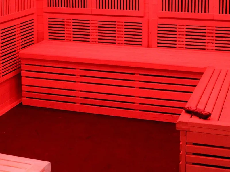 Interior of a red-lit sauna with wooden benches and slatted walls