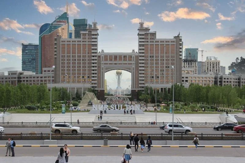 A tall brick and white building stands behind a busy street with a "Nur Sultan" sign.