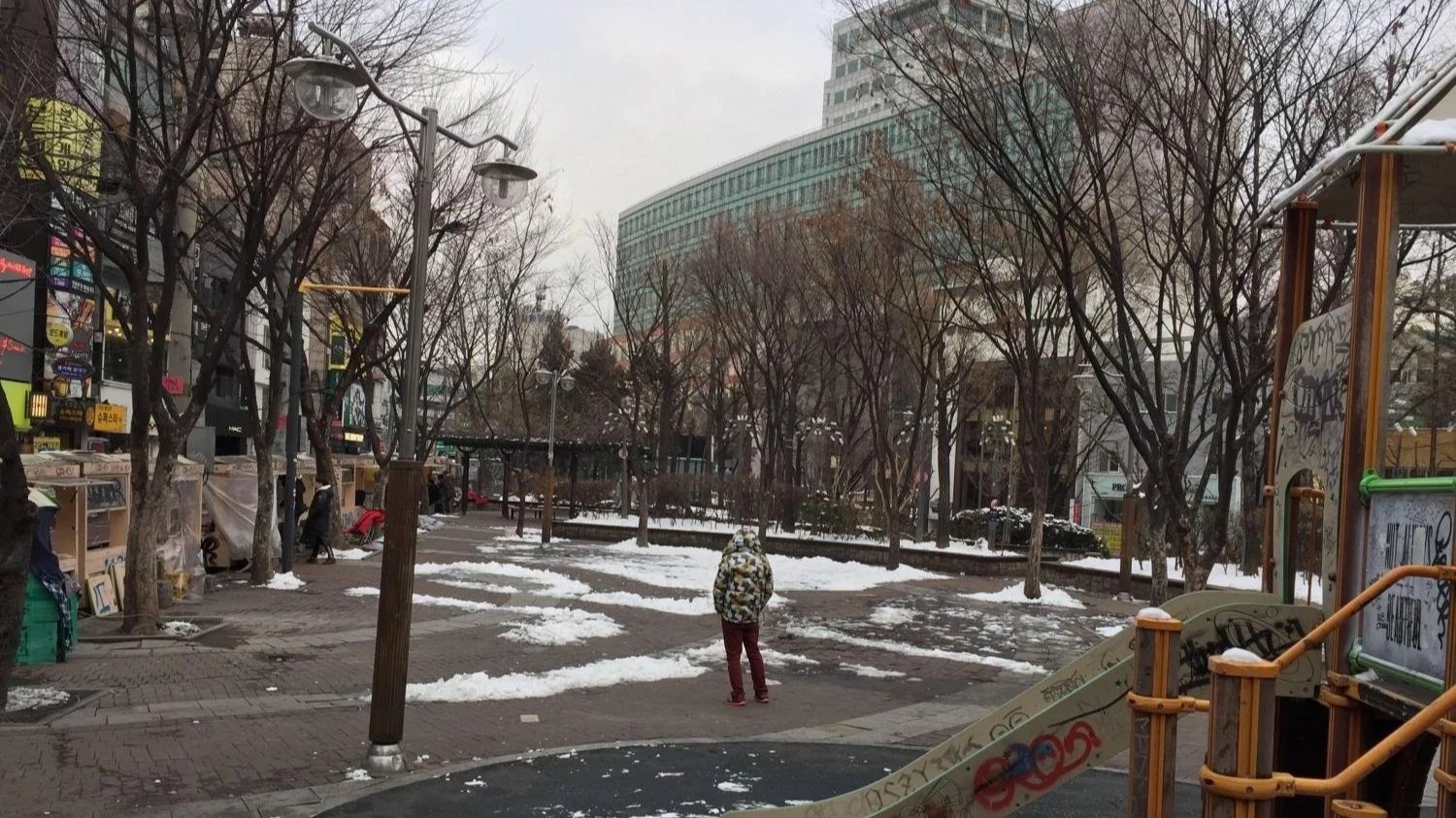 A man in a chekered jacket gazes out over a park in Seoul during winter.