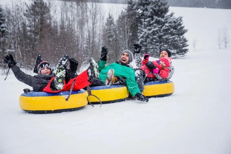 A family laughs and smiles as they tube down a snow-covered hill in Mont Tremblant.