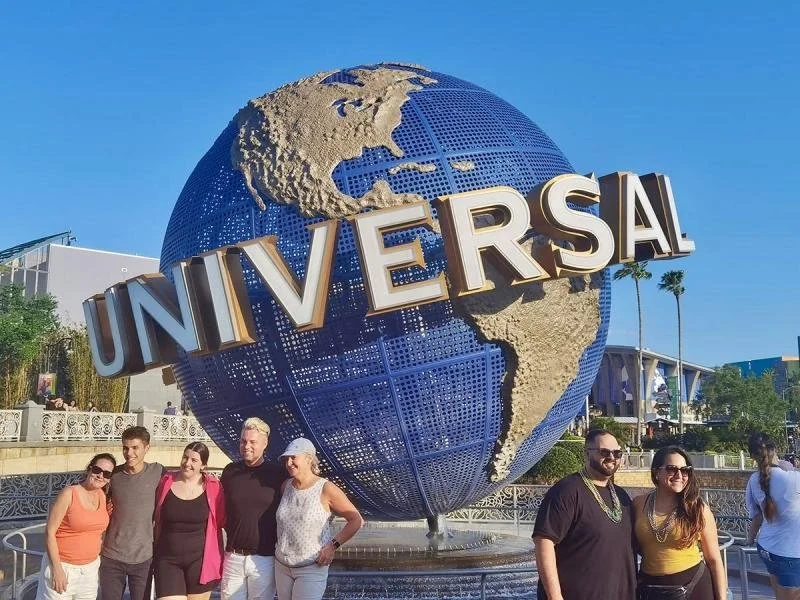 Tourists stand out front of a globe at the entrance of Universal Studios.
