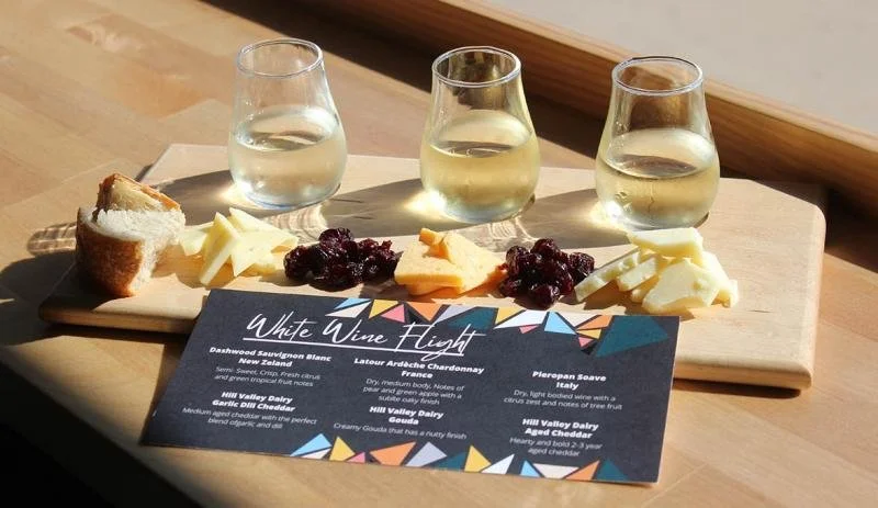 3 wine glasses sit on a board with raisons, bread and cheese at Hill Valley Cheese Shop and Bar.
