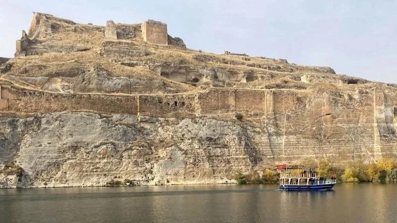 A boat passes on the Euphrates river alongside a Roman fortress.