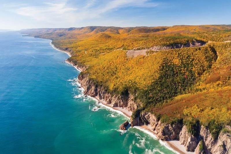 Bright blue water lap along the coastline of Cape Smokey during fall.