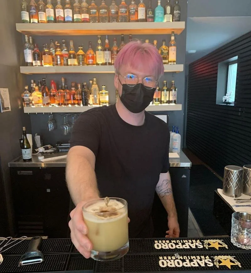 A pink haired bar tenders passes a "penicillin" cocktail
