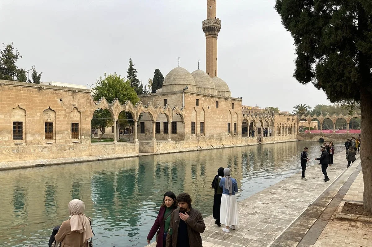 Passerbys in Balıklıgöl walk past a canal and an old mosque.