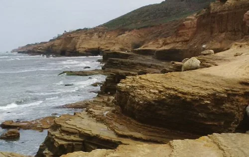 Waves lap against the rocks on a gray day in San Diego.
