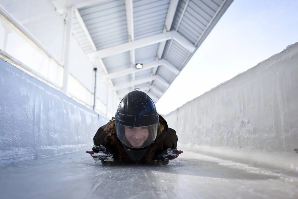 A girl wearing all black and a helmet slides on ice.