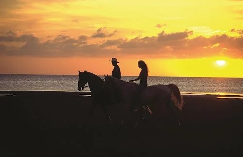 A couple rides on horses along the beach during sunset at South Padre Island.